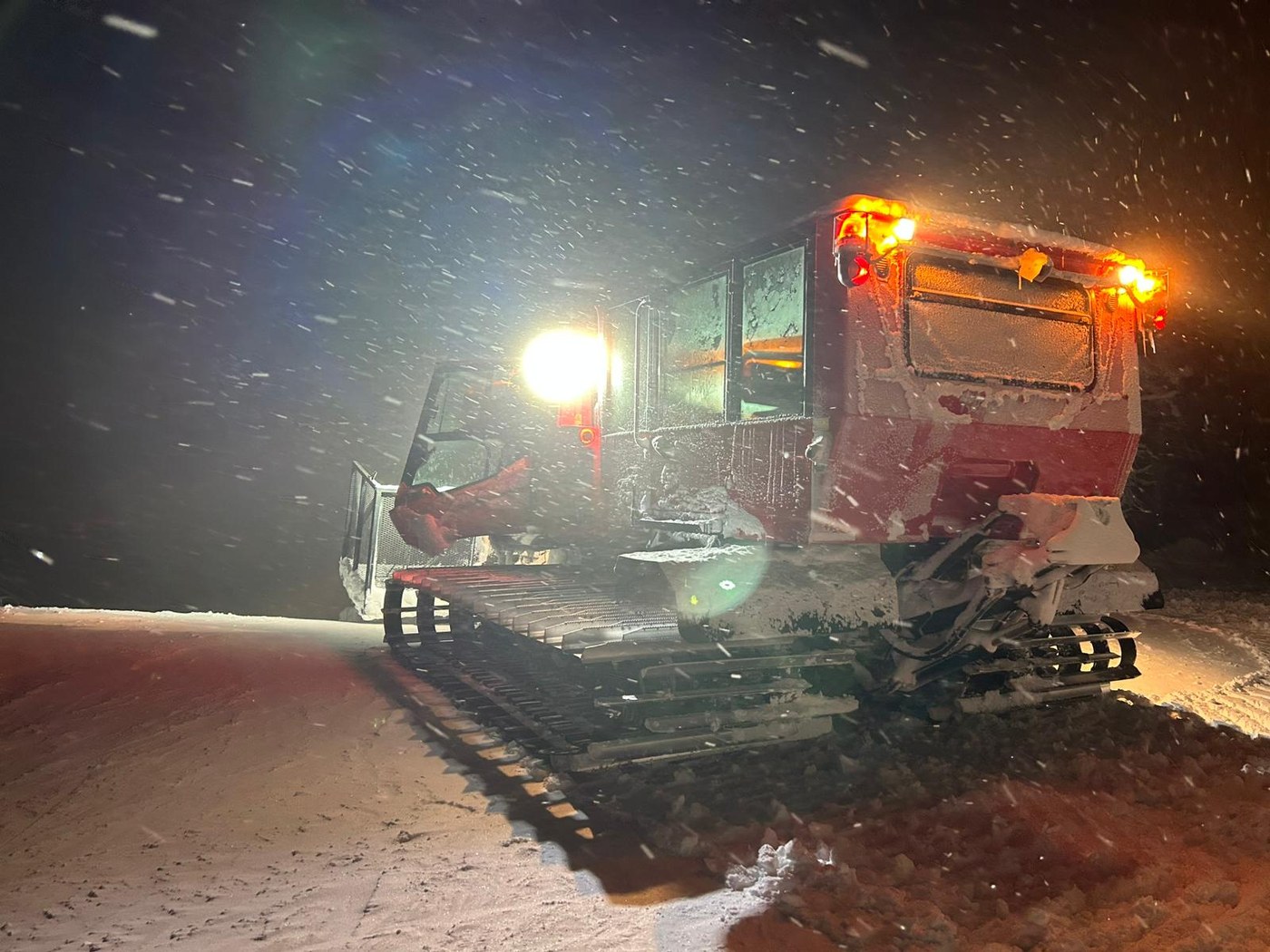 A red snowcat groomer with its beacons lit on a snowy night at Killington