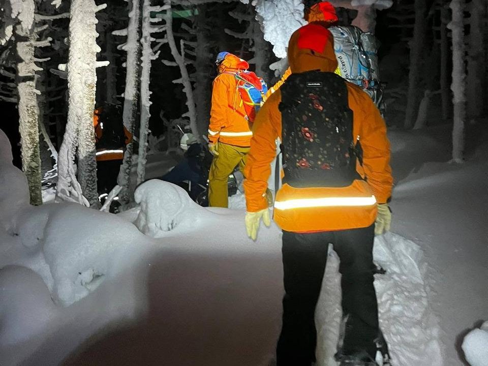 KSAR members in orange jackets and packs walk single file through snow-covered trees at night