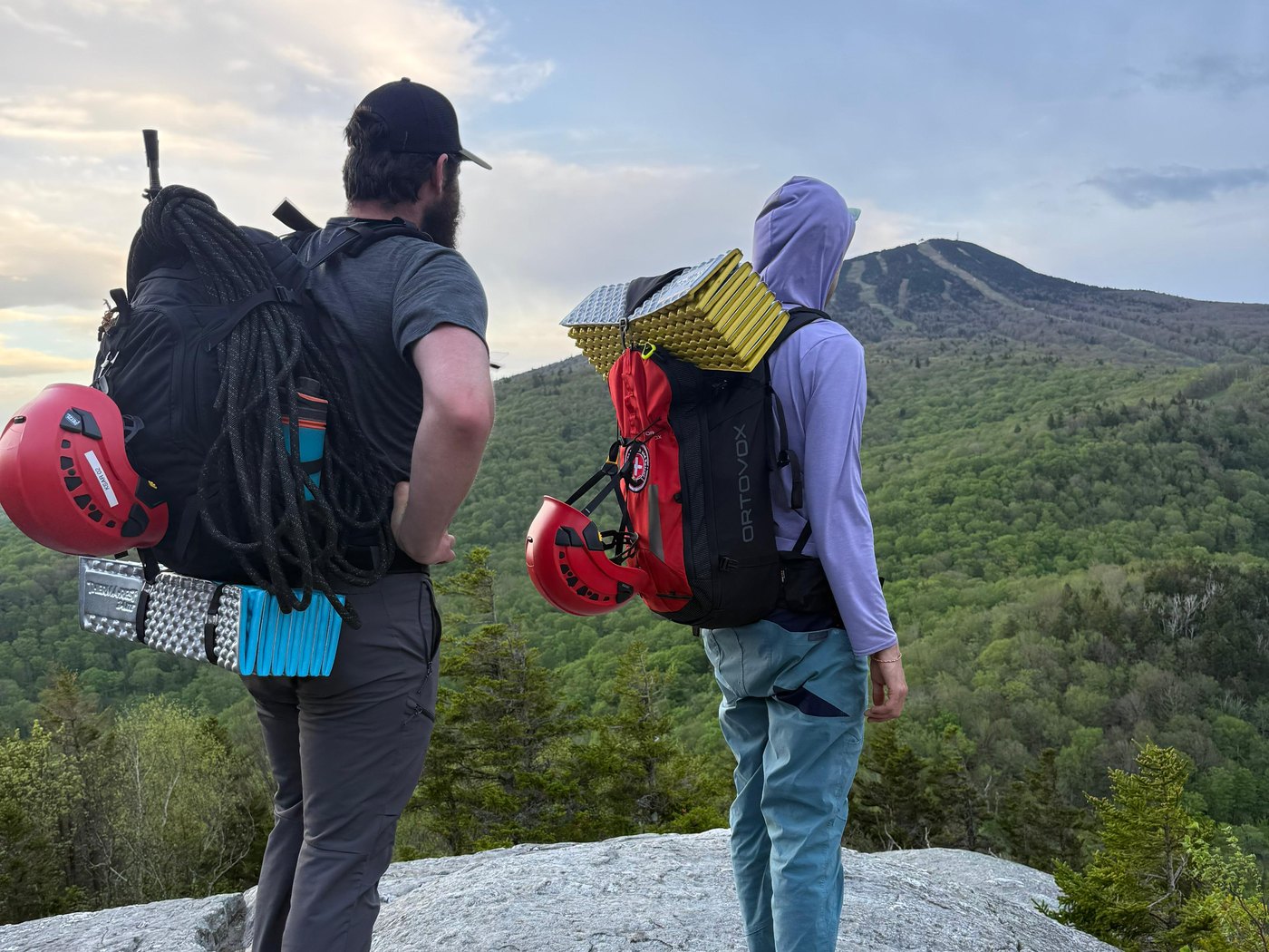 Two KSAR members with rope, helmets and packs look out from a ledge toward Killington Peak